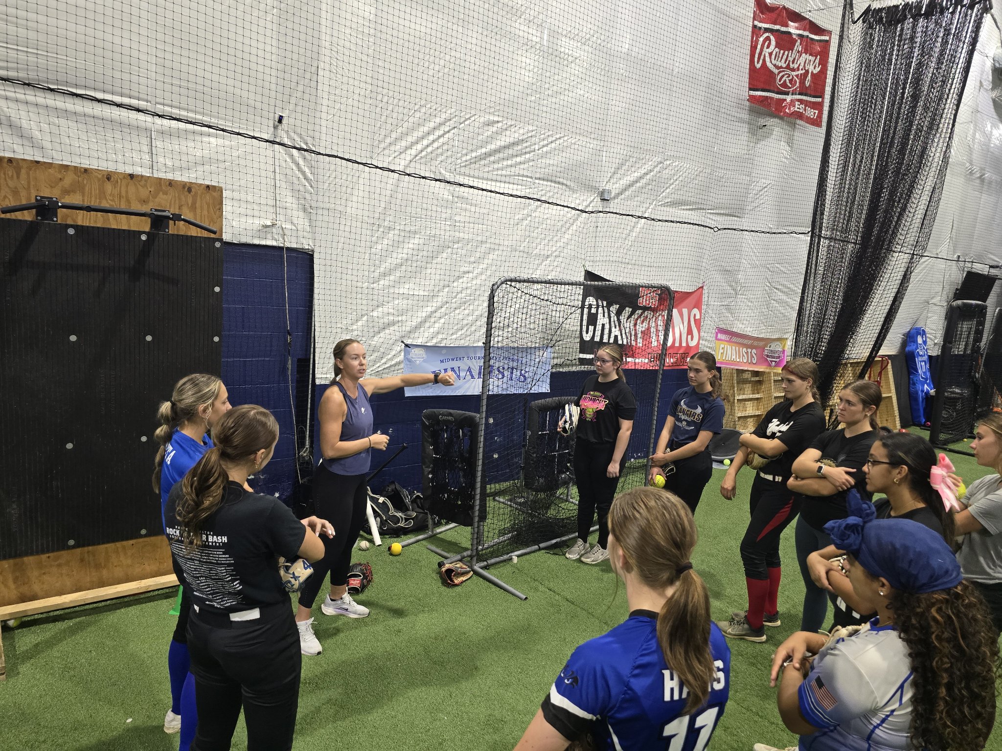 Jessie Harper pointing toward a drill while players listen beside a practice net