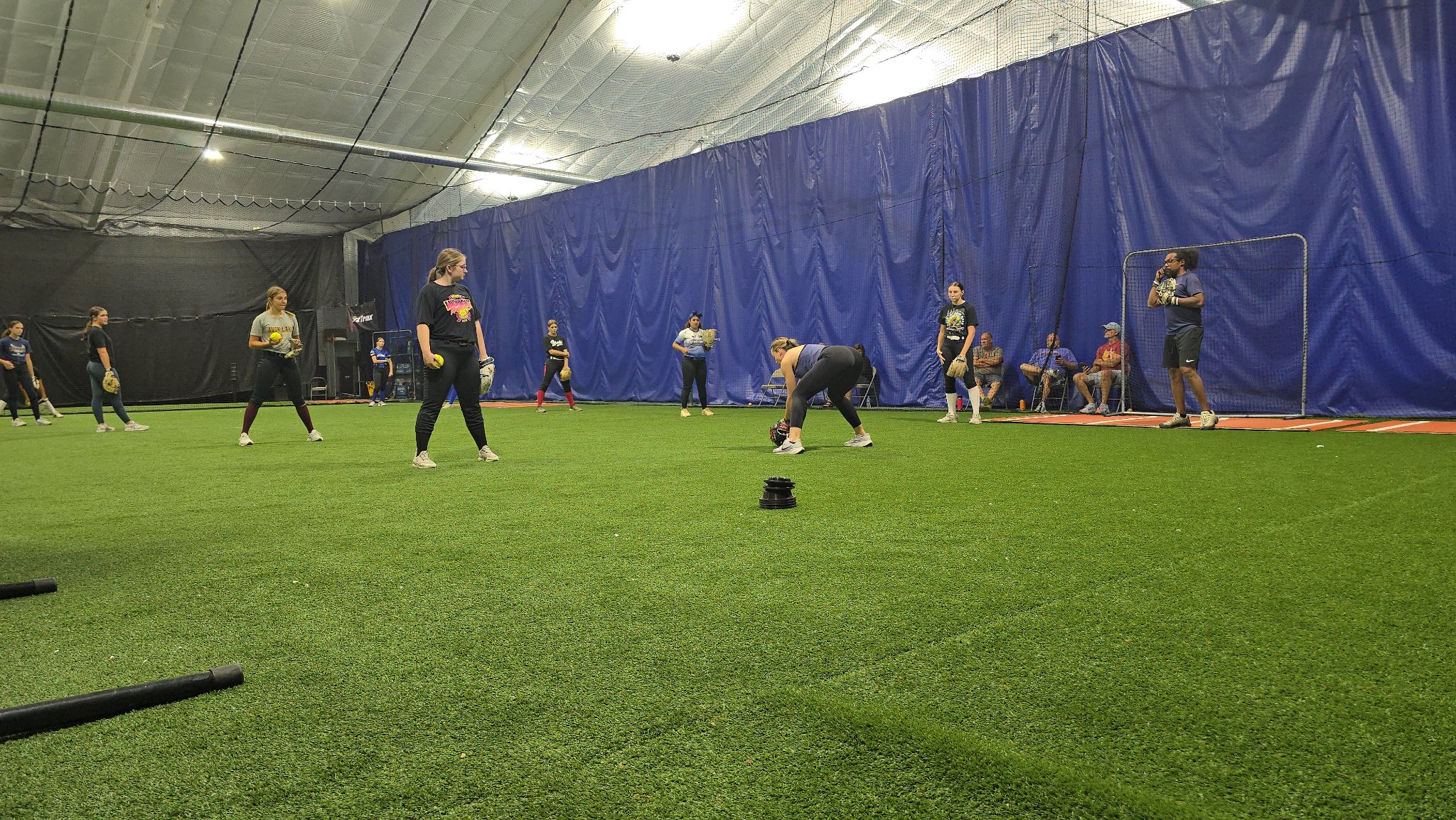 Softball players spaced across indoor turf during fielding drills