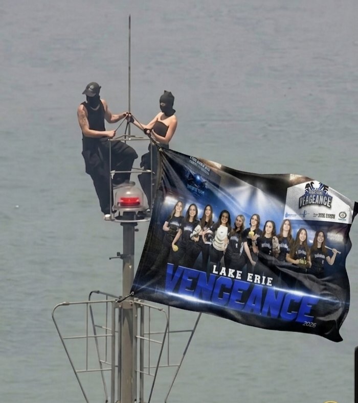 Two people hanging the Lake Erie Vengeance team banner from a tall tower over the water